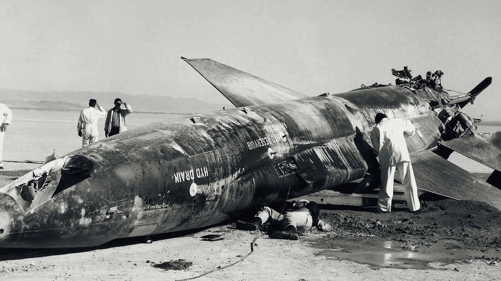 Black-and-white archive photograph of a damaged X-15 on the lakebed with ground crew
